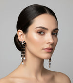 A pair of silver finish cubic zirconia flower drop earrings displayed on a stand, featuring a series of connected stones and flowers.