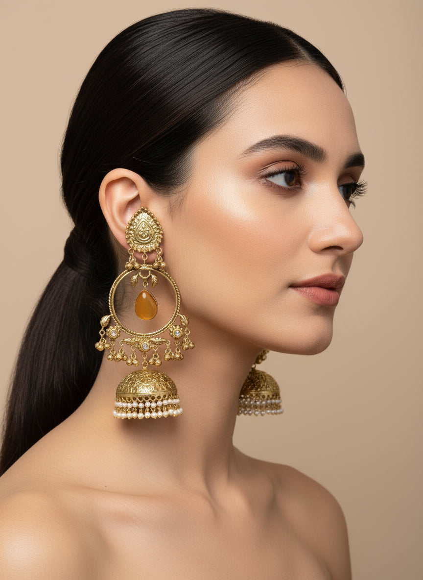 A pair of gold-plated long Jhumka earrings with intricate designs, dangling gems, and pearl accents on a black background