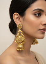 A pair of gold-plated long Jhumka earrings with intricate traditional design and miniature bells, displayed on a stand.