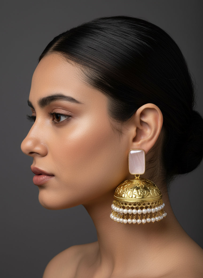 A pair of gold-colored Jhumkas earrings featuring intricate designs, dangling gems, and pearl accents, displayed against a dark background.