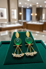 A pair of gold-plated Mona Lisa pendulum earrings featuring green stones and silver pearls.