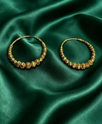 Pair of Famaza Couture 22K gold-plated beaded hoop earrings resting on rich emerald green satin; features graduated filigree beads, intricate openwork detailing, chand bali inspired luxury design — premium Pakistani jewelry.