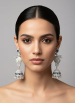 A pair of silver finish American diamond drop Jhumka earrings displayed on a stand.