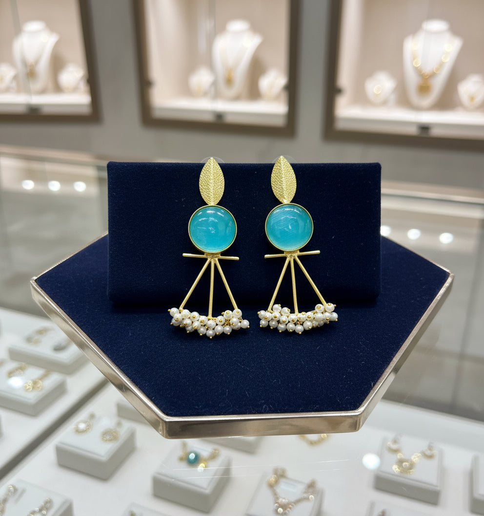 A pair of gold-plated Mona Lisa pendulum earrings featuring green stones and silver pearls.