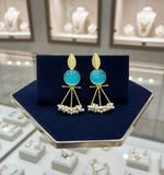 A pair of gold-plated Mona Lisa pendulum earrings featuring green stones and silver pearls.