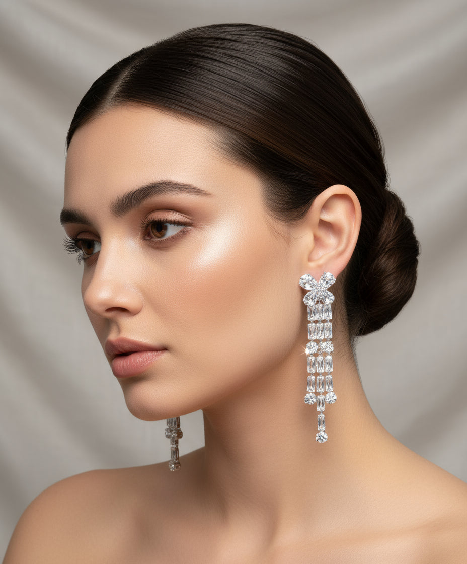 A pair of silver finish cubic zirconia flower drop earrings displayed on a stand, featuring a series of connected stones and flowers.