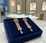 A pair of silver finish cubic zirconia flower drop earrings displayed on a stand, featuring a series of connected stones and flowers.