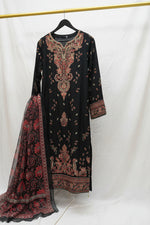 A black long kurta with intricate red, orange, and gold embroidery hanging on a yellow clothing rack inside a retail store. Other colorful garments are visible in the background.