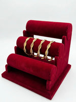 A set of four three-tone micro gold-plated copper bangles featuring an intricate floral lattice and scalloped eyelet design in yellow, white, and pink gold finishes, displayed on a tiered red velvet jewelry stand.