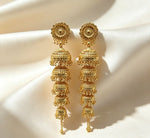 Pair of 5-tier cascading gold jhumka earrings with filigree rosette tops and five descending domed bells, handcrafted gold-plated traditional South Asian bridal statement jewelry on cream satin background.