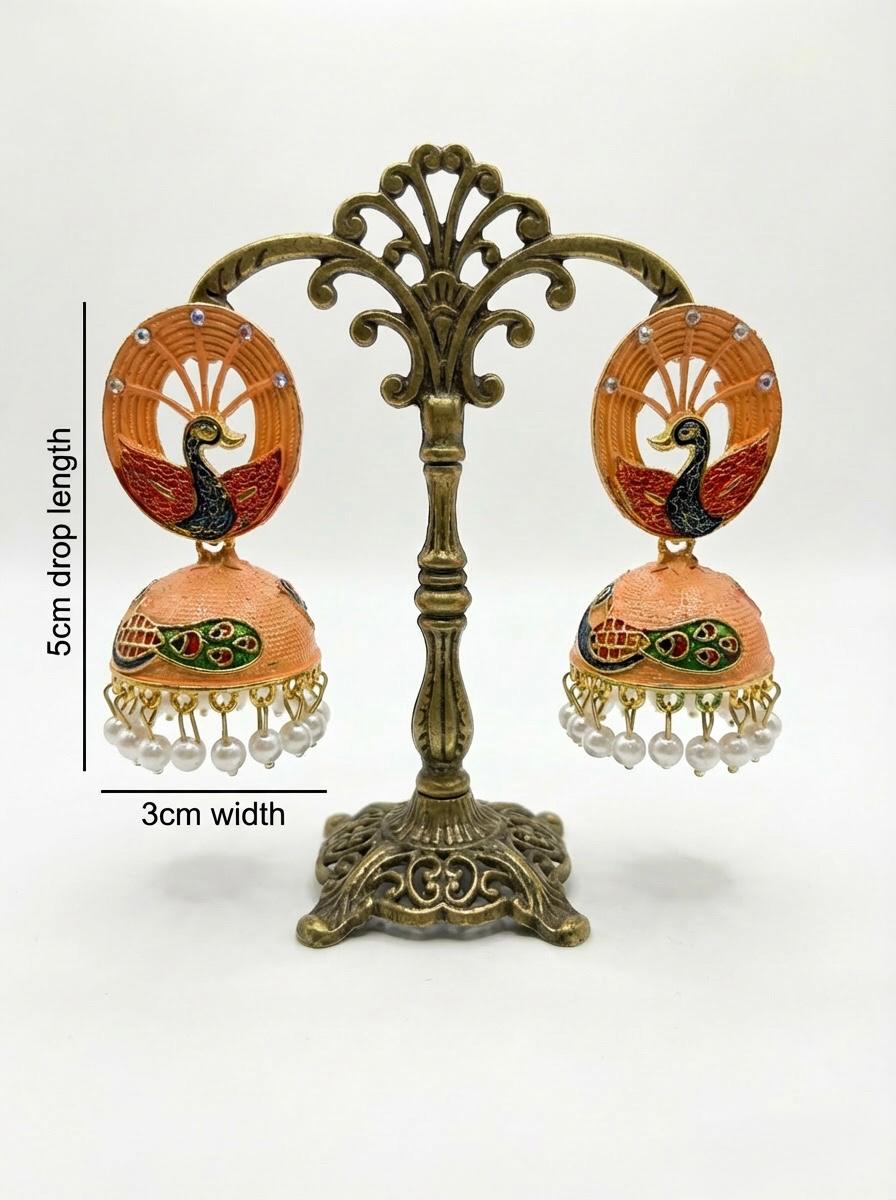 5.5cm orange Meenakari peacock jhumkas with hand-painted enamel and white pearl fringe on a professional stand.