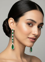 A pair of silver finish American diamond Jhumka bali earrings with green and clear stones on a stand.