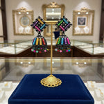 A pair of black multi-colored stone earrings on a stand, featuring a geometric pattern and dangling with small beads.