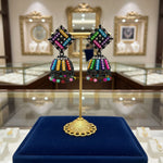 A pair of black multi-colored stone earrings on a stand, featuring a geometric pattern and dangling with small beads.