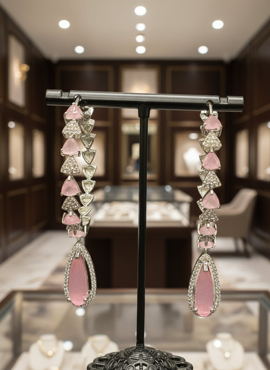 A pair of silver finish American diamond Jhumka bali earrings with green and clear stones on a stand.