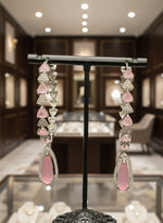 A pair of silver finish American diamond Jhumka bali earrings with green and clear stones on a stand.