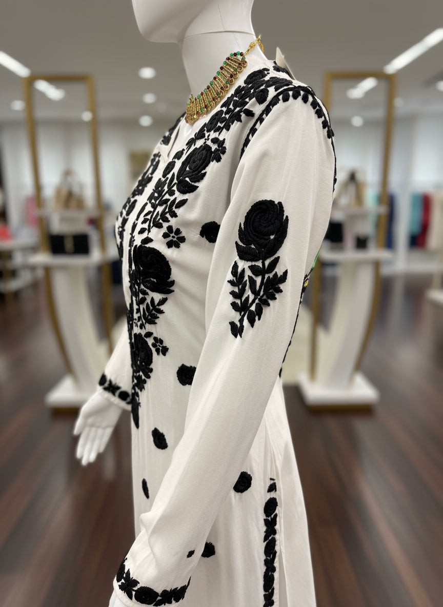 White dress with black floral embroidery on a mannequin against a white background