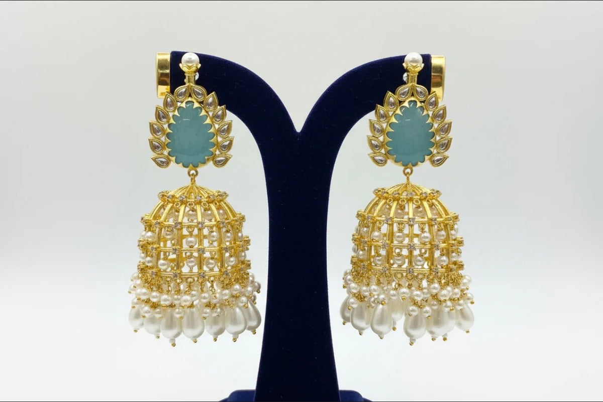 Gold and pearl earrings on a black stand with a white background.