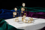 Gold earrings with pearl-like stones on a marble surface with colorful fabric background
