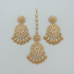 A Rose Gold-toned Indian bridal jewellery set featuring a maang tikka and twodangle earrings all embellished with intricate crystal work and hanging tassels, displayed on a black posh velvet surface.