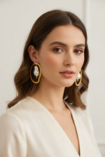 A Woman wearing gold hoop earrings with mother of pearls hanging freely in the middle of the hoop