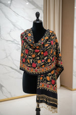 A black pashmina scarf with Kashmiri embroidery in a floral pattern, featuring tassels on the ends.