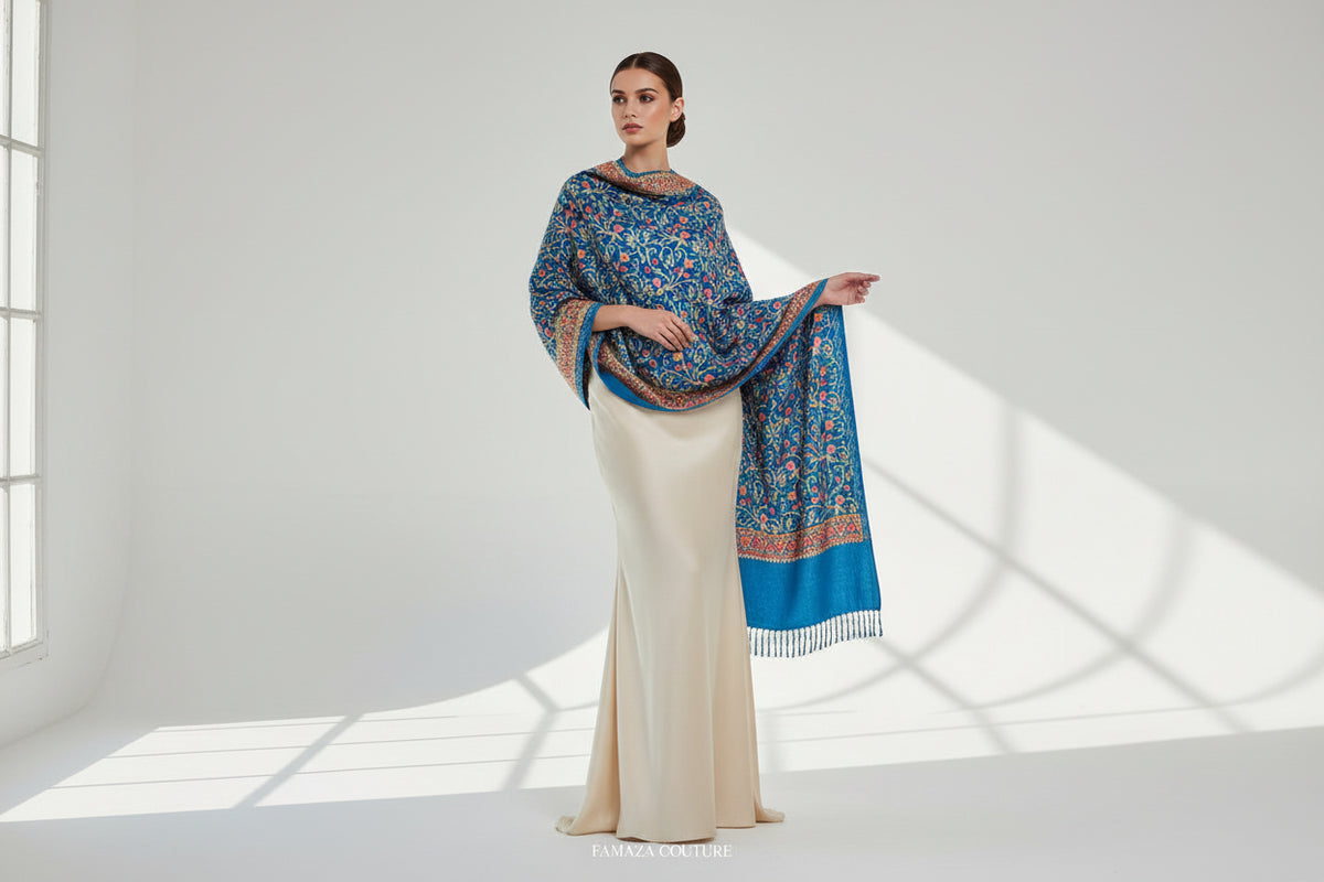 A blue Kashmiri embroidered pashmina scarf with tassels hanging at the ends, displayed on a wooden surface.