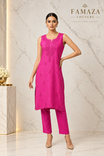 A woman modeling a bright pink kurta and matching trouser set against a white marble-patterned studio backdrop.