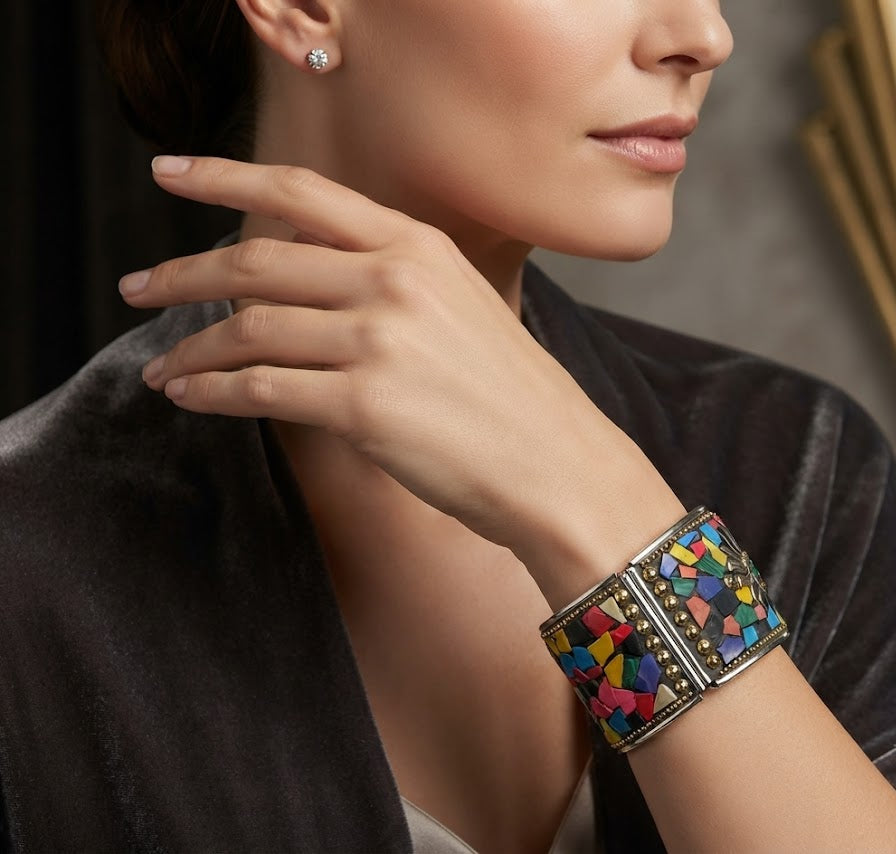 A close-up lifestyle shot of a woman wearing a wide silver-toned cuff bracelet decorated with a vibrant mosaic of colourful geometric shapes, paired with a matching stud earring.