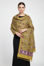 A close-up of Mustard base colour Kashmiri embroidered pashmina scarf with maple leaf motifs and tassels on the ends, displayed on a wooden surface.