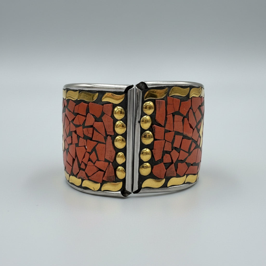 A close-up of a decorative cuff bracelet featuring a mosaic pattern of terracotta red tiles and gold-coloured metallic accents, set against a black velvet-like background.