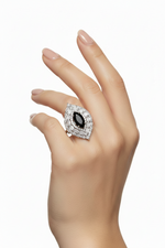 A close-up of a hand wearing a large teardrop-shaped ring with a central clear gemstone surrounded by multiple rows of small clear stones in a silver-toned setting, against a plain white background.