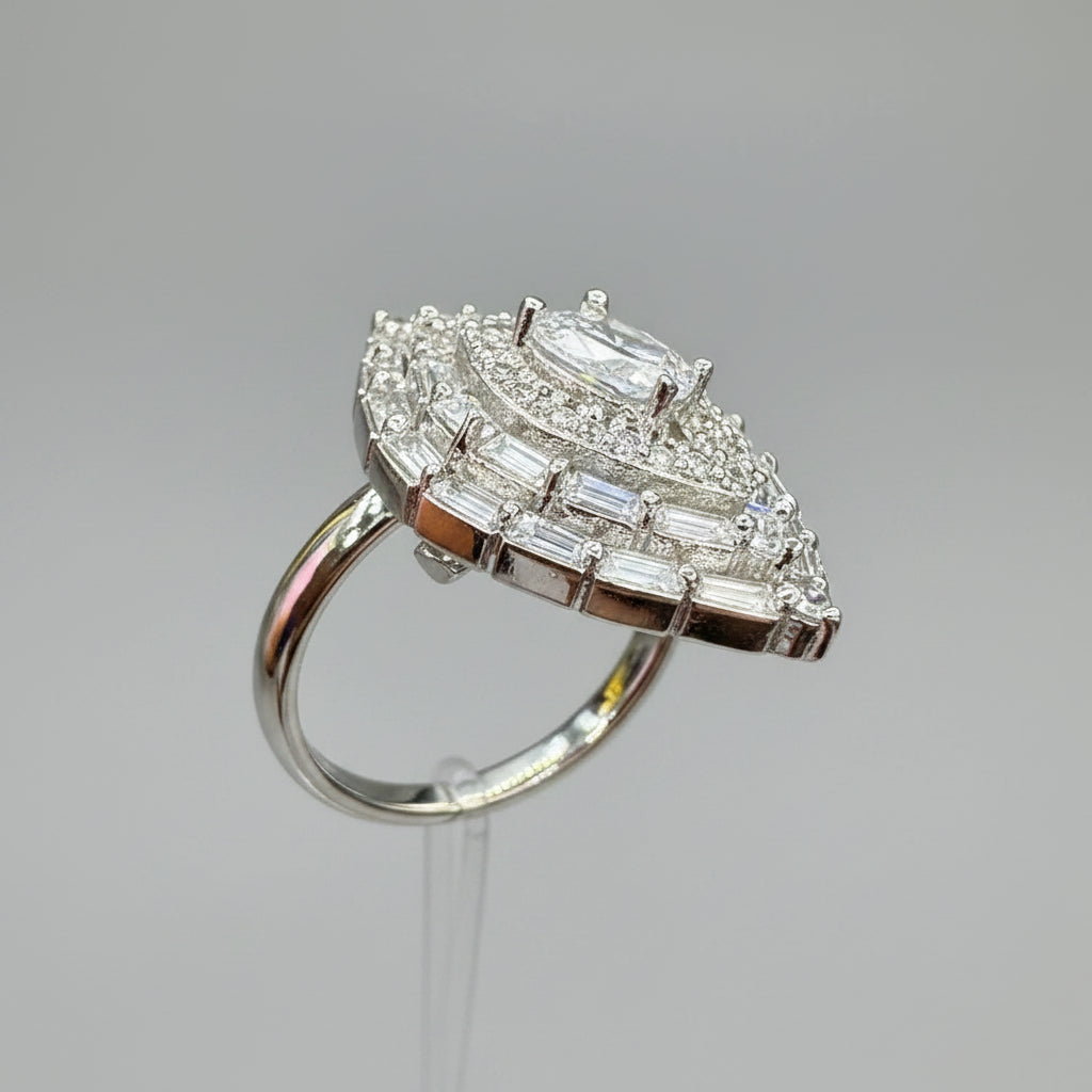 A close-up of a hand holding a silver-toned ring with a large, intricate cluster of clear gemstones on a polished band, set against a blurred indoor background.