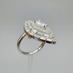 A close-up of a hand holding a silver-toned ring with a large, intricate cluster of clear gemstones on a polished band, set against a blurred indoor background.