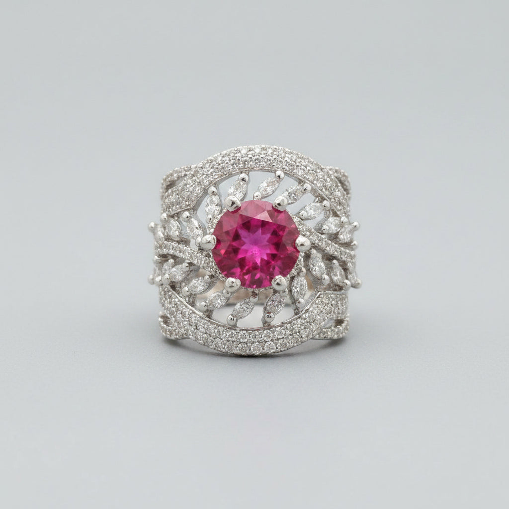 A close-up of a hand holding a silver ring with a round pink gemstone and small clear stones around it, set against a dark textured background.