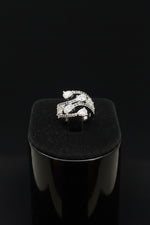 A close-up of a hand wearing a silver snake-themed ring set with clear pavé stones, shown against a black background.