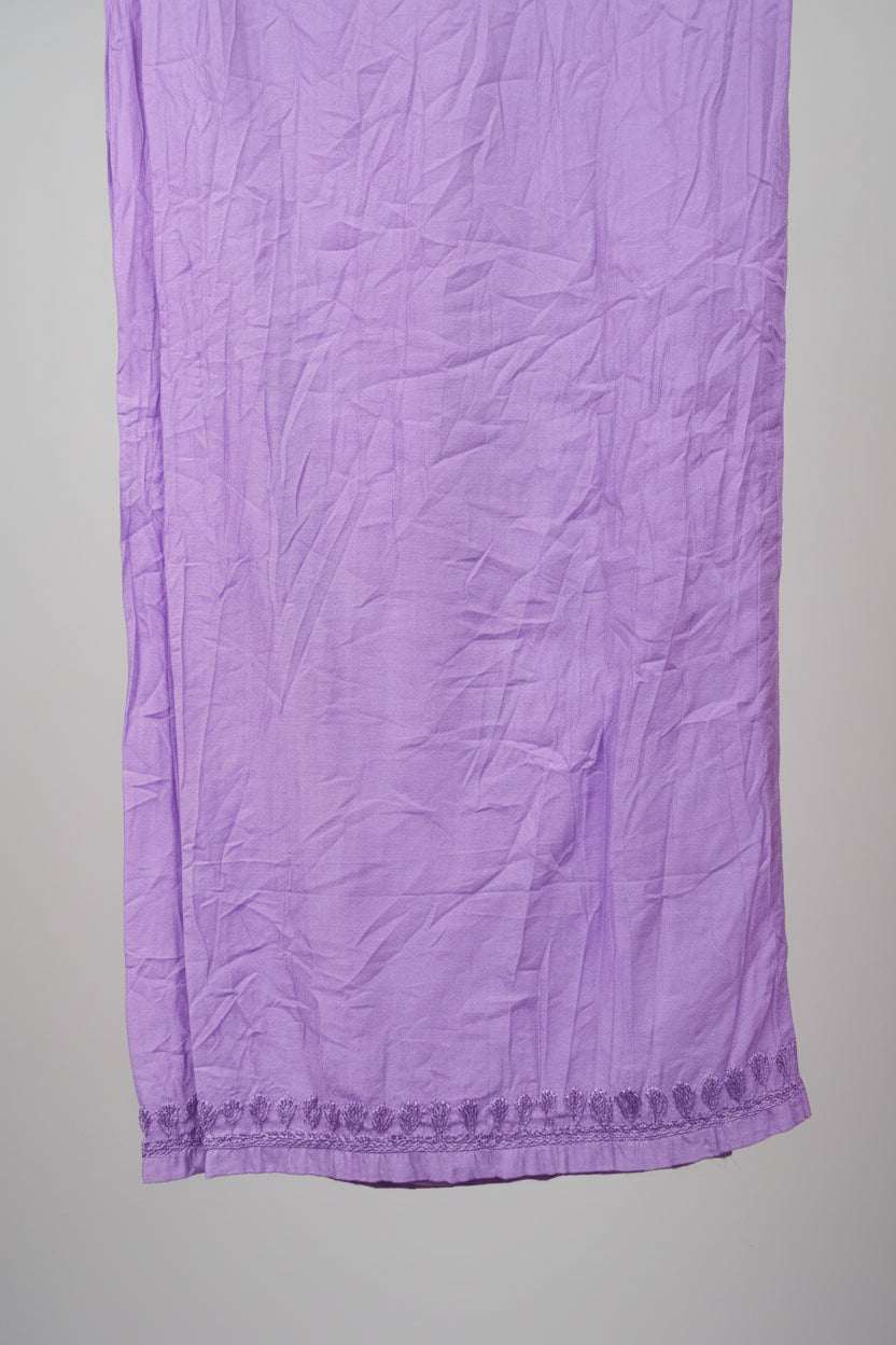 A close-up of a lavender purple textured fabric, likely a scarf, sash, or decorative textile, hanging vertically. The fabric features a subtle woven pattern and a decorative embroidered or lace-like border along the bottom edge.