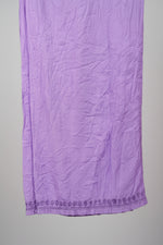 A close-up of a lavender purple textured fabric, likely a scarf, sash, or decorative textile, hanging vertically. The fabric features a subtle woven pattern and a decorative embroidered or lace-like border along the bottom edge.