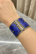 A close-up of a silver cuff bracelet with a mosaic blue lapis lazuli and gold accents, worn on a person's wrist.