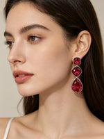 A close-up of a woman wearing a dangling earring with three stacked teardrop-shaped red gemstones in silver-toned settings.