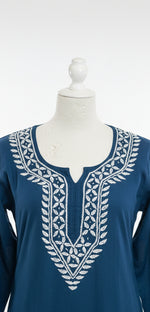 Adeep sea blue tunic dress with white geometric embroidery around the neckline, sleeve cuffs is in focus for famaza couture website.