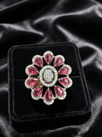 A floral-shaped silver ring with pink gemstones and clear stones, displayed on a black velvet jewelry box against a black satin background.