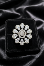 A silver-tone floral ring with clear gemstones, displayed on a black velvet jewelry box over a black satin fabric background.