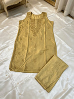 A gold-coloured traditional Indian salwar suit set consisting of a sleeveless kurta with embroidered neckline and matching trousers, laid flat on a white satin sheet.