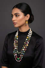 A gold-plated Kundan-studded and pearl-beaded handcrafted jewellery set, consisting of a necklace and earrings, displayed against a black background.
