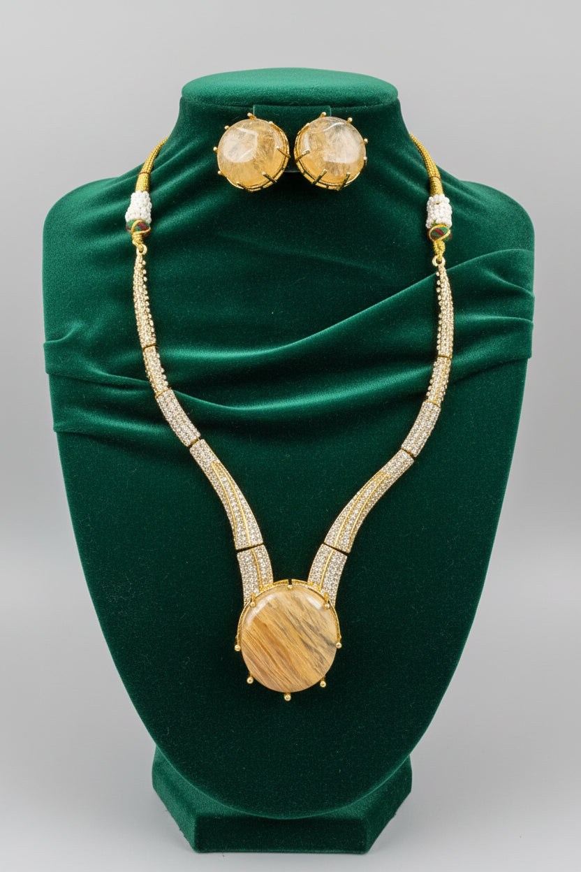 A gold-tone necklace and matching stud earrings displayed on a black velvet jewellery bust. The necklace features a large oval wooden pendant, textured round gold-toned studs, and small white bead accents.