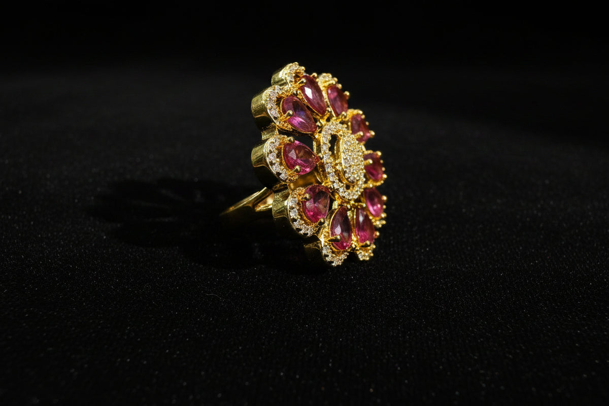 A gold flower-shaped finger Ring with pink teardrop gemstones and a textured gold centre, displayed on a white faux fur surface.