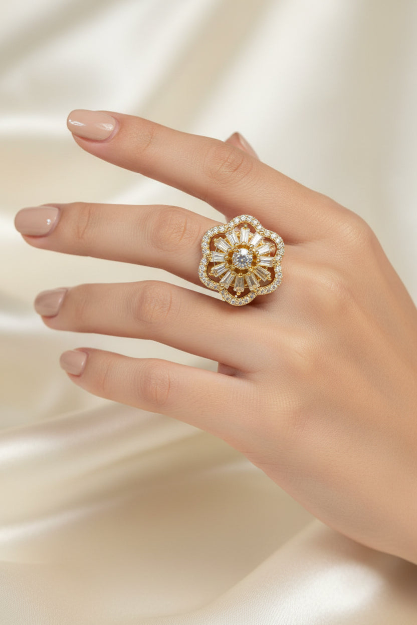 A gold flower-shaped ring with a central round diamond and surrounding baguette and round stones, held on a black display cone.