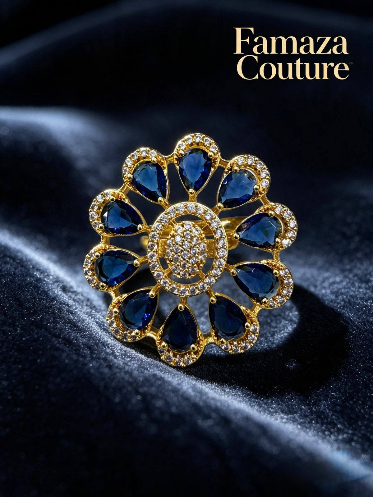 A gold flower-shaped ring with deep blue teardrop gemstones and a central cluster of small clear stones, displayed on a dark velvet surface. The brand name 'Famaza Couture' is visible in the top right corner.
