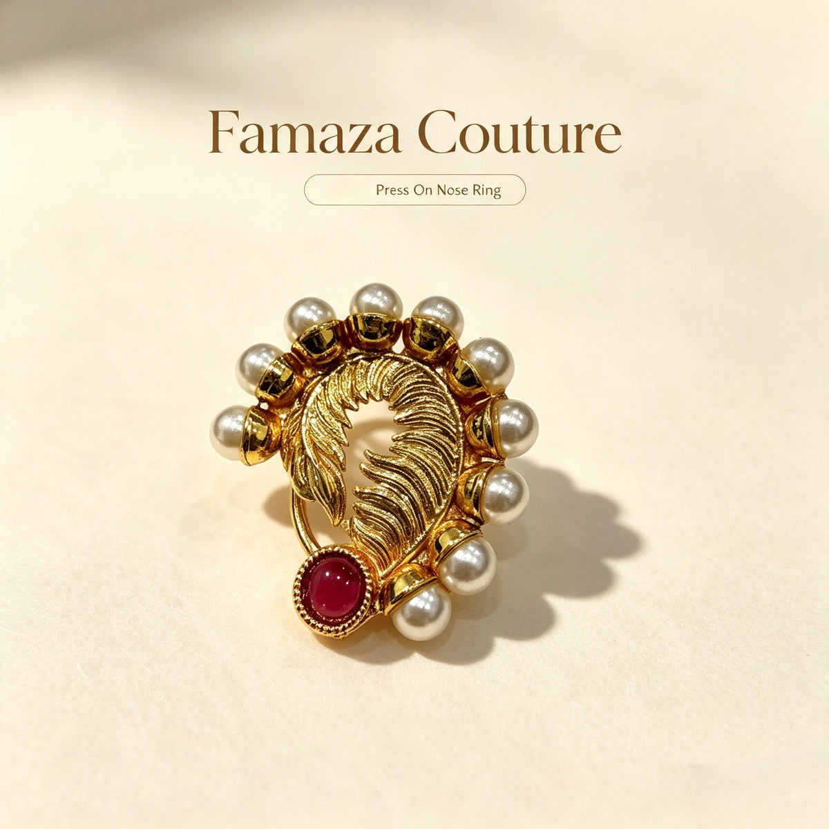 A gold nose ring styled like a feather with white pearl beads and a red gemstone, displayed on a beige background with the text 'Famaza Couture' and 'Press On Nose Ring'.